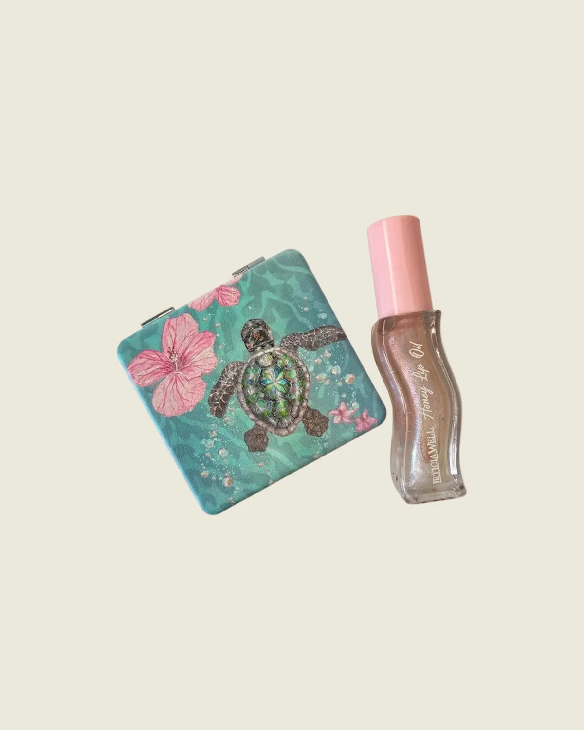 Miroir de poche à motif tortue marine et fleurs roses, posé à côté d’un gloss