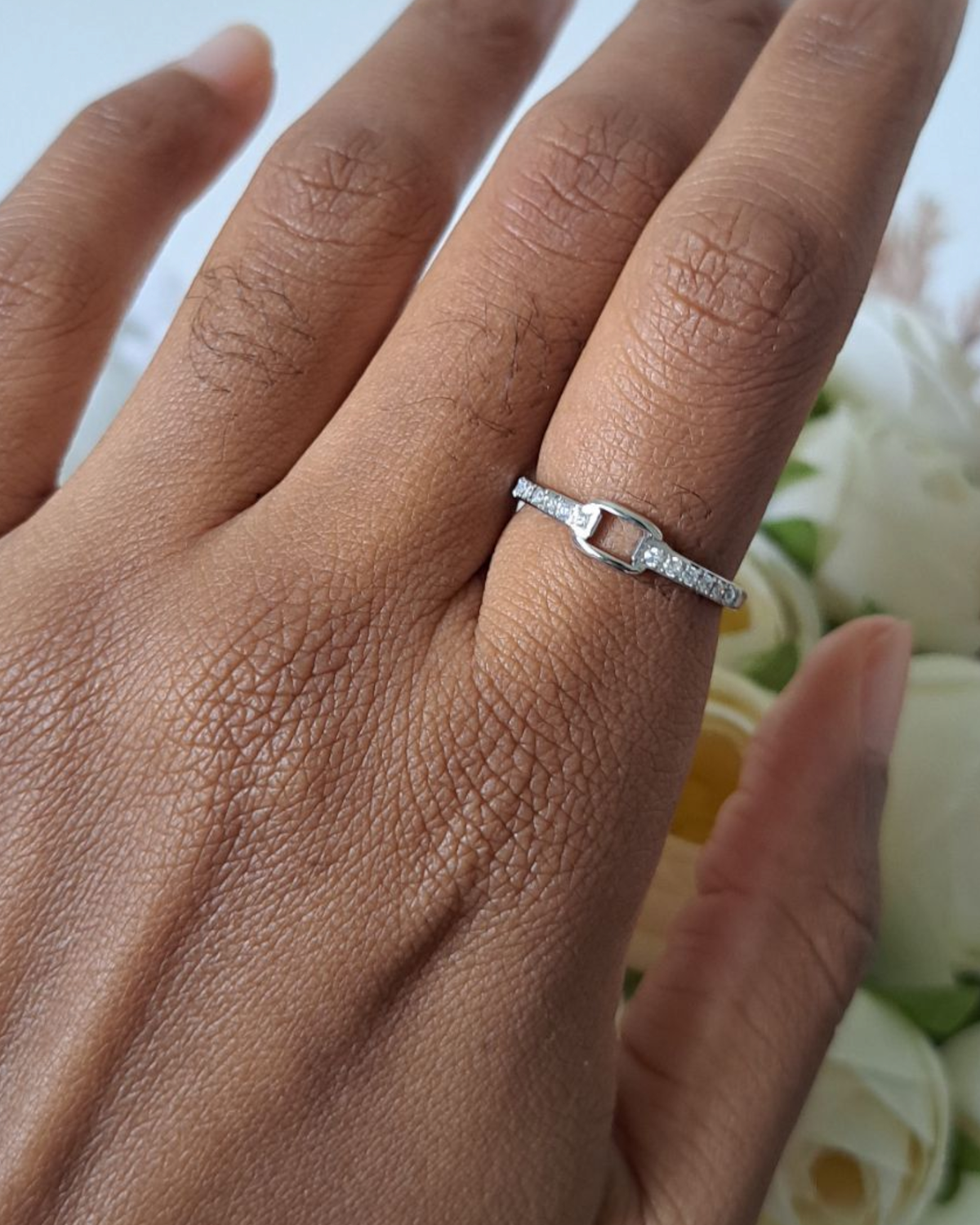 Bague strass argentée portée au doigt devant des fleurs blanches – bague fine zirconium femme