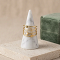 Bague astrale en acier inoxydable doré à plusieurs rangs, ornée d’étoiles et d’un détail blanc nacré, sur un présentoir conique