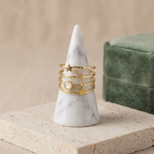 Bague astrale en acier inoxydable doré à plusieurs rangs, ornée d’étoiles et d’un détail blanc nacré, sur un présentoir conique