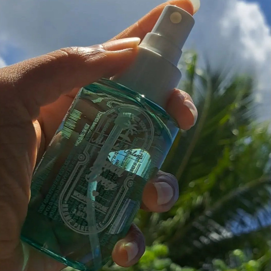 Brume parfumée Tropical Breeze tenue en main sous les palmiers – parfum femme tropical