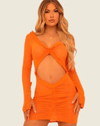 Robe courte orange portée de face, avec manches longues, découpe au ventre et finitions à volants.