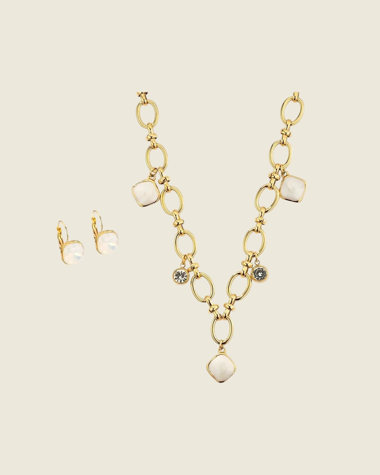 Parure dorée composée d'un collier chaîne à maillons avec pendentifs en pierre blanche et cristaux, et boucles d'oreilles assorties à cabochon nacré