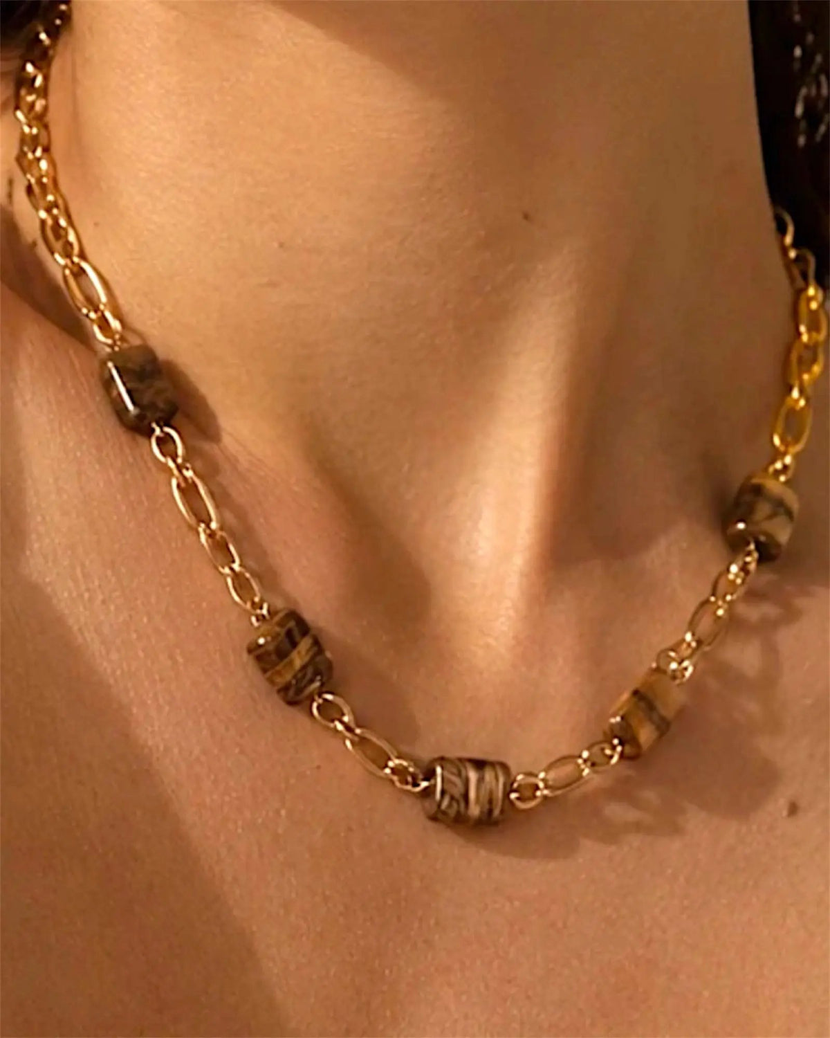 Collier chaîne dorée avec perles en œil de tigre porté par une femme, style naturel beach-luxe
