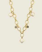 Collier chaîne dorée à maillons porté sur une femme, avec pendentifs en pierre de lune blanche et cristaux, style beach-luxe