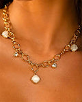 Collier chaîne dorée à maillons porté sur une femme, avec pendentifs en pierre de lune blanche et cristaux, style beach-luxe