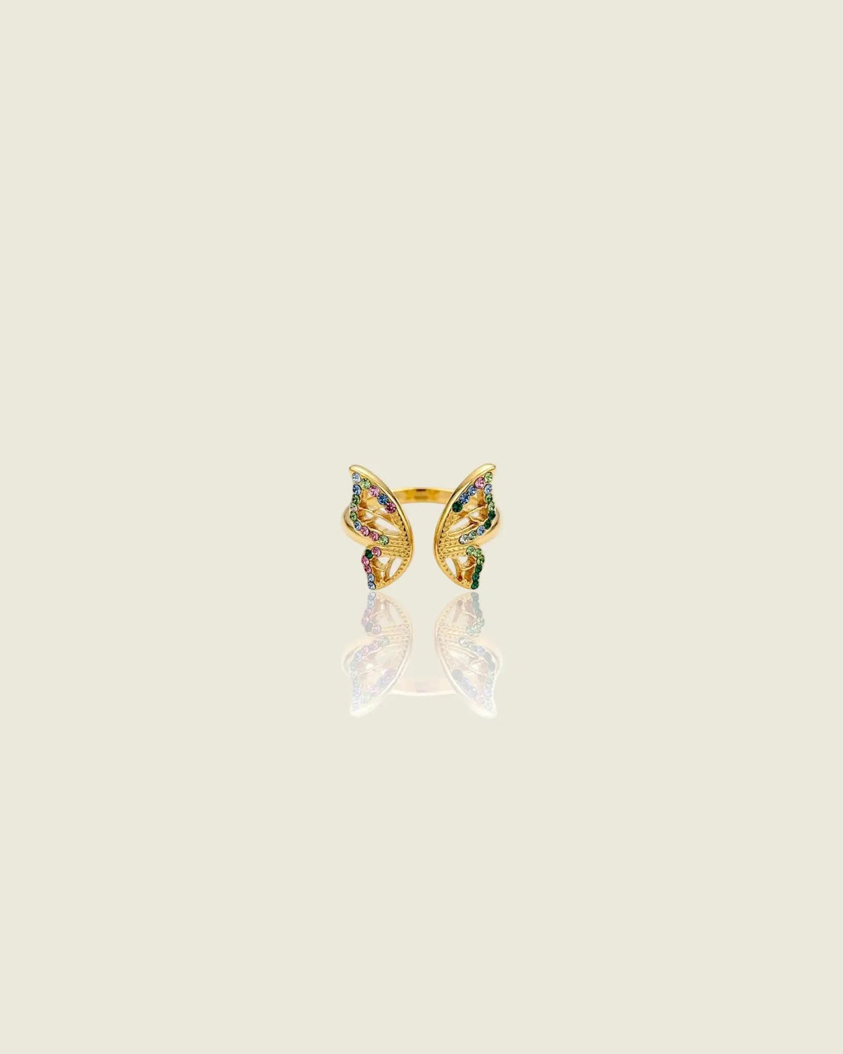 Bague ouverte dorée en forme de papillon, ornée de pierres multicolores, sur fond beige avec reflet.