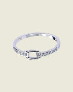 Gros plan de la bague fine argentée, montrant les strass de chaque côté du motif carré ajouré, sur fond beige clair