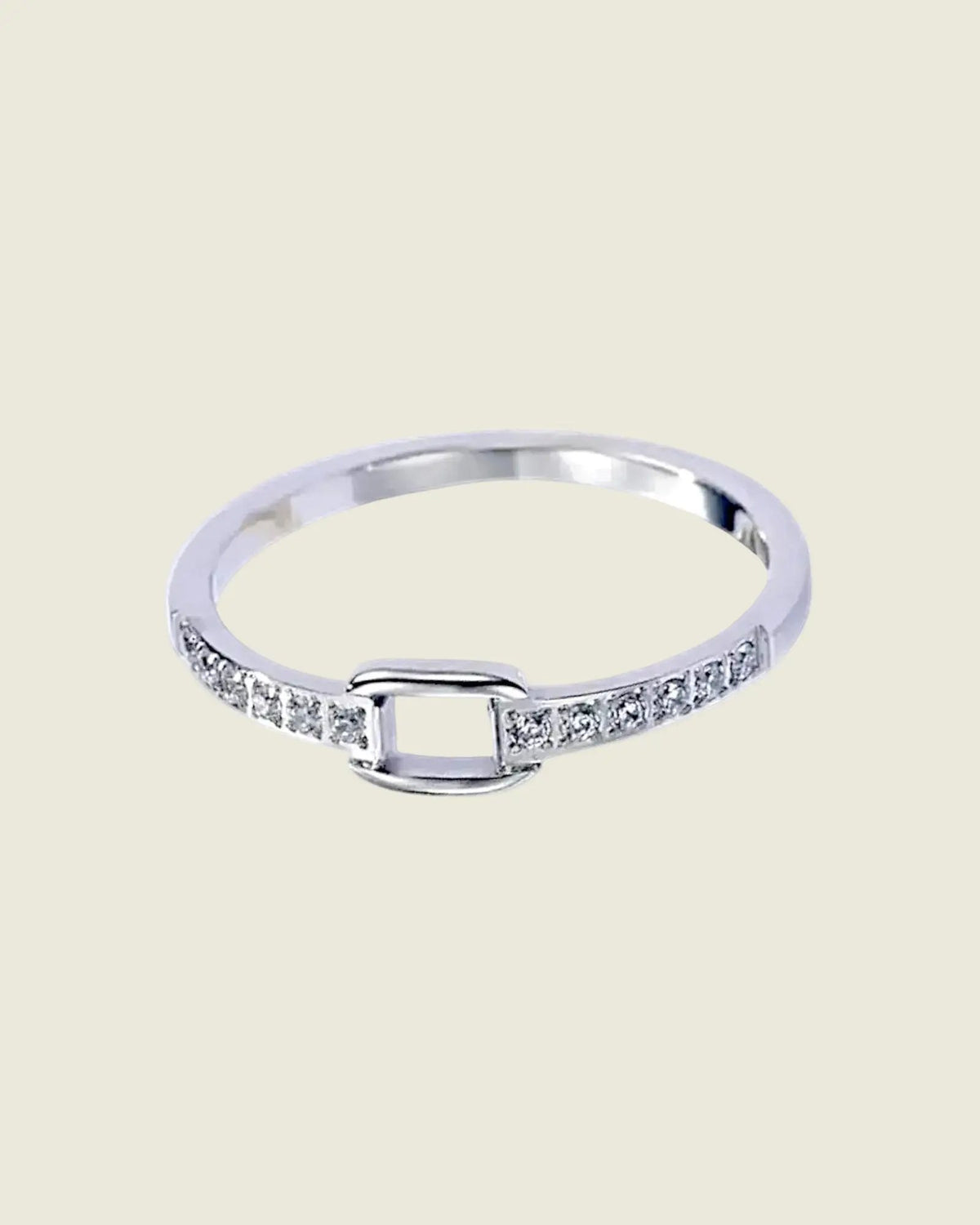 Gros plan de la bague fine argentée, montrant les strass de chaque côté du motif carré ajouré, sur fond beige clair