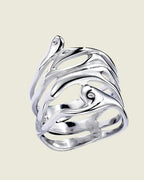 Gros plan de la bague large ajourée en acier inoxydable argenté, montrant son design organique sur fond beige clair