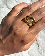 Bague dorée motif entrelacé portée au doigt sur fond de rocher – bijou femme acier inoxydable