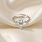 Bague réglable en acier inoxydable argenté ornée de pierres de zirconium en forme de goutte et de petits strass, sur un tissu satiné ivoire