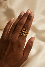 Bague large dorée au design organique ajouré, portée à l’index sur un fond de tissu beige